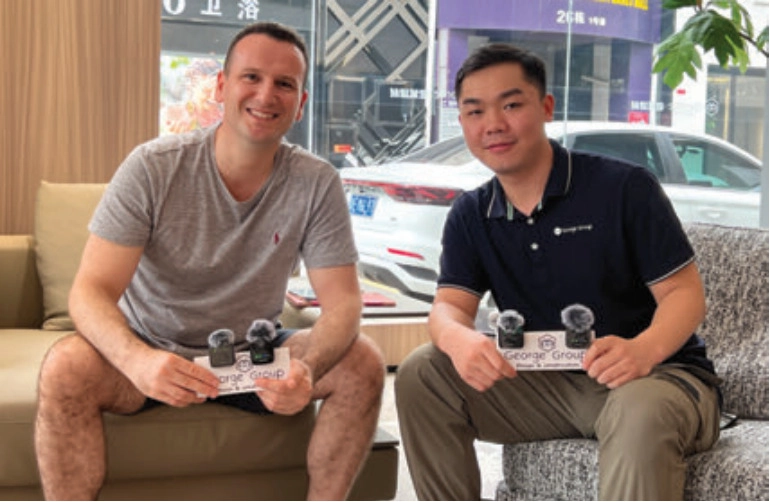Two men seated in a showroom holding George Group cards and small microphones