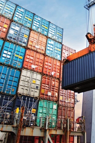 Stacks of multicolored shipping containers with a blue container suspended by lifting equipment