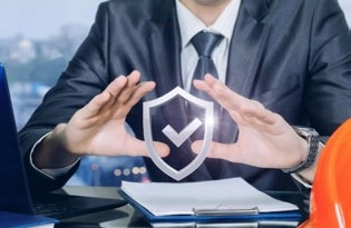 Person in a suit gesturing around a shield graphic with a check mark, beside a clipboard and hard hat