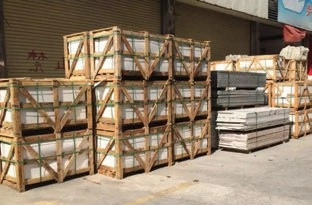 Wooden crates secured with green straps and stacks of flat panels outside warehouse roller doors