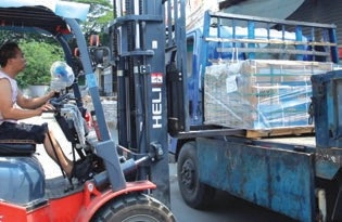 Forklift operator lifting a wrapped pallet beside a blue open-sided truck