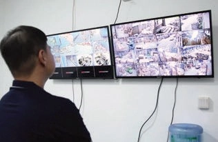 Man watching two wall-mounted monitors showing multiple warehouse camera views