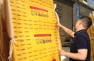 Man reaching toward a tall panel wrapped in yellow protective packaging beside a warehouse roller door