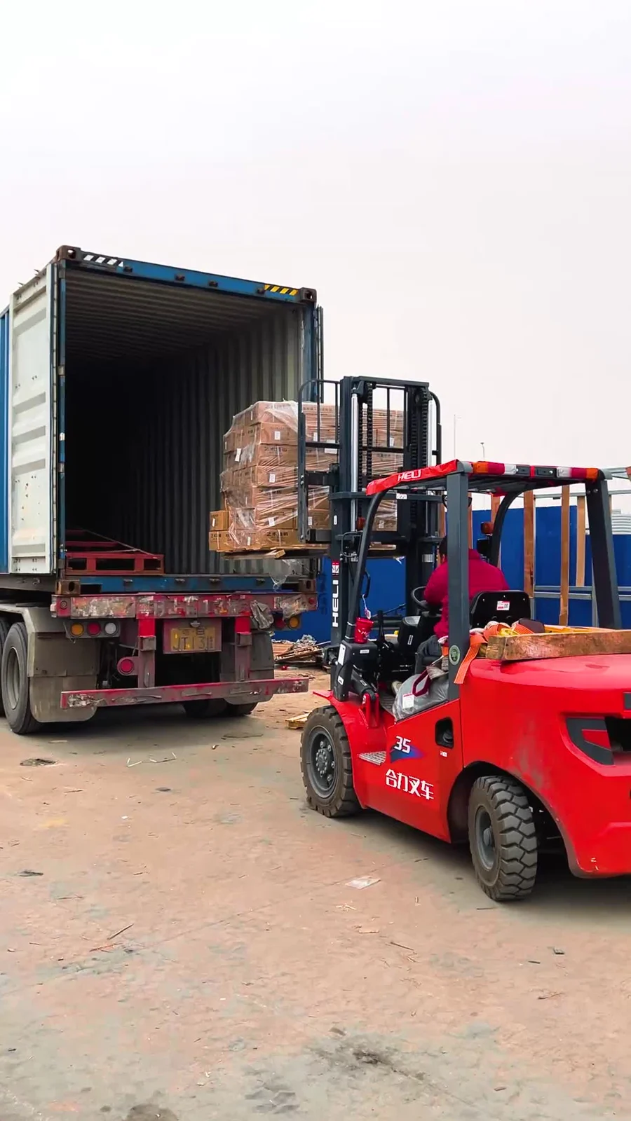 Forklift lifting a wrapped pallet into an open shipping container at the loading yard