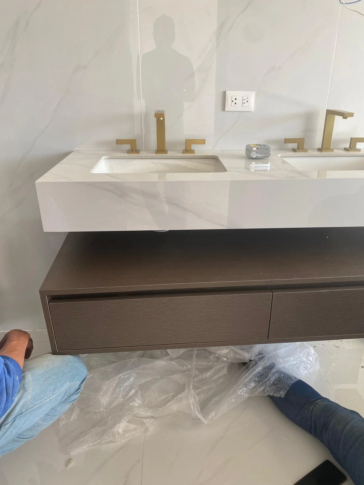 Wall-mounted vanity with a pale veined basin top, wood-tone drawers and brass-coloured faucets